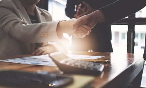 A taxpayer assisted by a tax professional shaking hands with an IRS agent in an office.