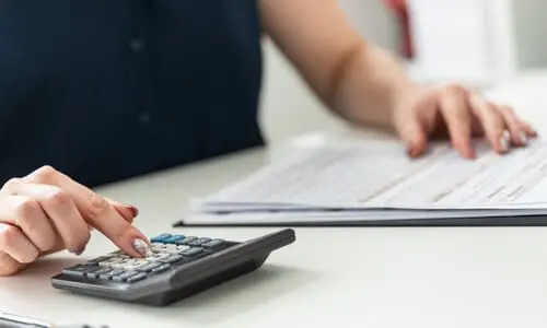 A woman computing how much she owes to the IRS with a calculator and a pen and paper.