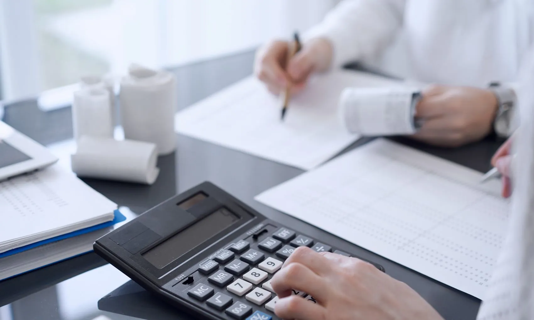 A depth of field shot of a calculator on a desk with a tax professional working in the background.