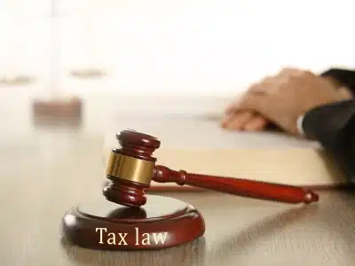 A wooden gavel hammer engraved with the words ‘Tax Law,’ with a blurred figure of an Aurora tax lawyer in the background.