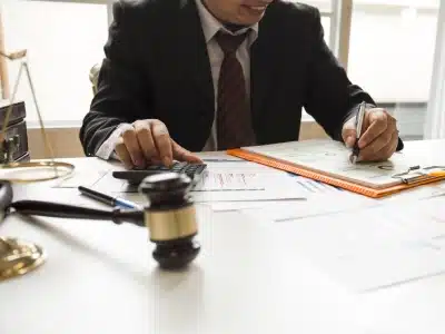 A broomfield tax lawyer using a calculator in the right hand while writing down on a notebook in the left hand while sitting in a law office