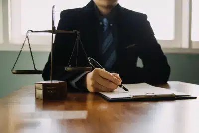 A tax lawyer serving Del Aire sits upright while signing a document placed on a clipboard lying beside balance scales