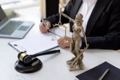 An image of a tax lawyer serving Lennox who is sitting at a table with a laptop and a statue as they sign a document placed on a clipboard